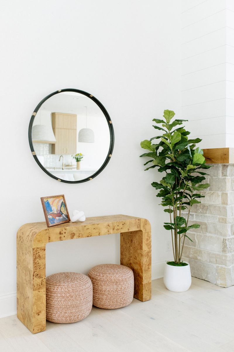 A white entryway in Panora with a round black mirror above a burl wood console table.