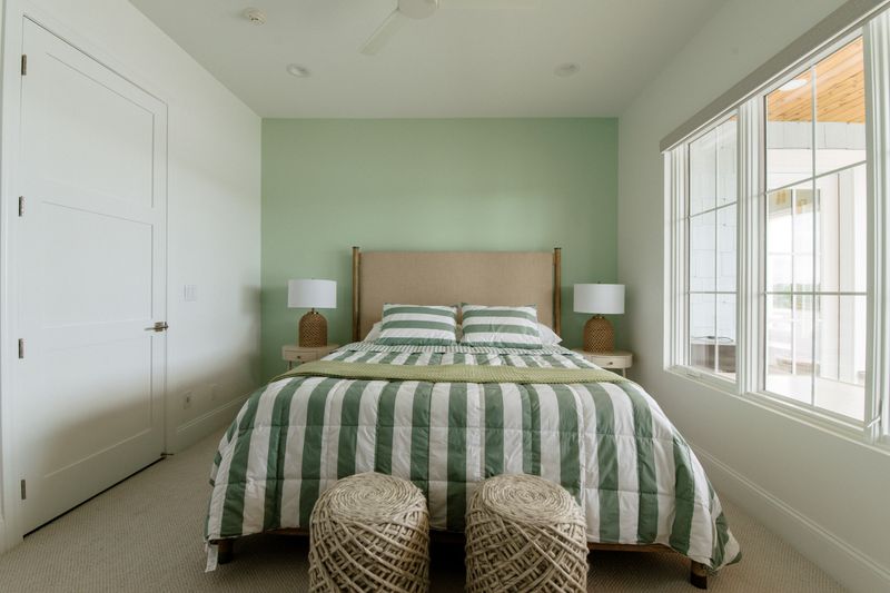 A guest bedroom in Panora with a sage green accent wall and a green and white striped bed.