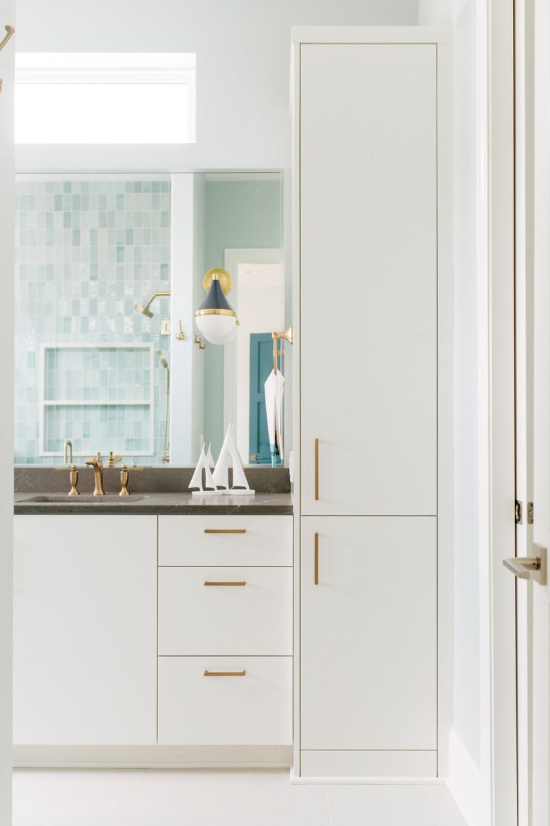 A kids bath in Panora with aqua glass tile behind the shower and brass hardware on flat white cabinets.