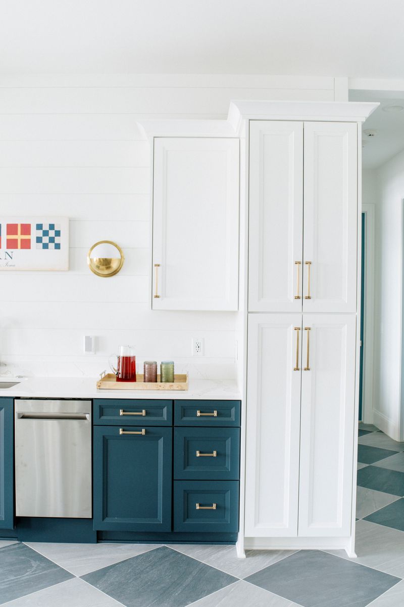 A kitchen in Panora with teal lower cabinets and brass pulls above a green and gray checkerboard tile floor.