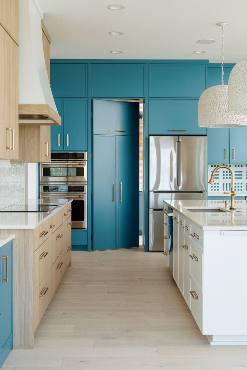 A kitchen in Panora with teal cabinets running to the ceiling and brass pulls on a white oak island.