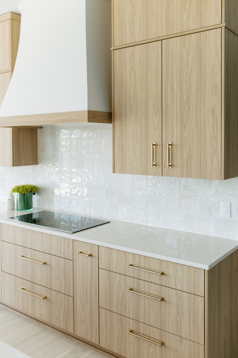 A white oak kitchen in Panora with a glossy white tile backsplash running behind the cooktop.