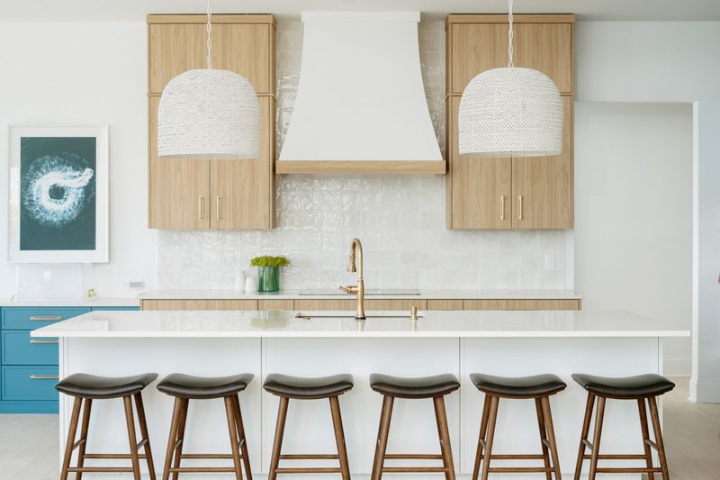 A white kitchen in Panora with a woven pendant over the island and white oak cabinets beside a plaster hood.