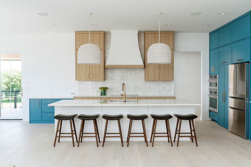 A white oak kitchen in Panora with a plaster hood over glossy white tile, above teal lower cabinets.