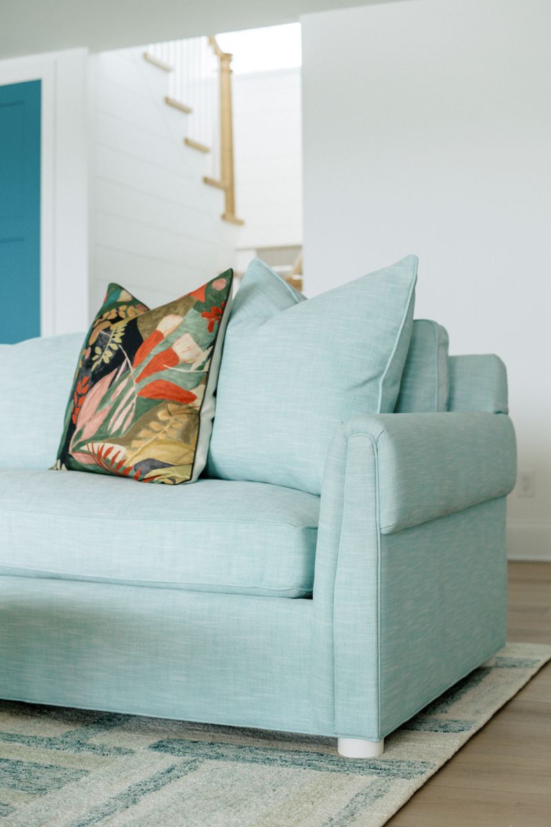 A living room in Panora with a pale aqua linen sofa and a botanical print pillow against white shiplap.