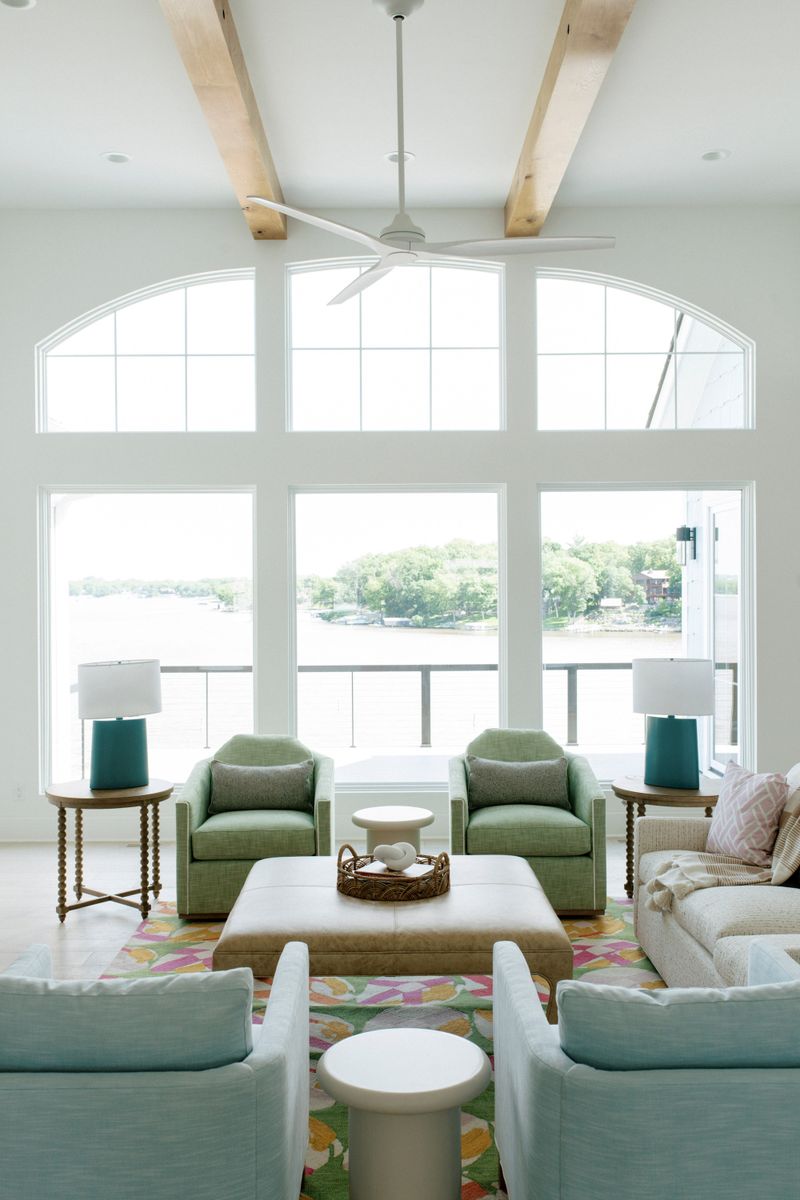 A lakeside living room in Panora with green swivel chairs around a tan leather ottoman on a floral rug.