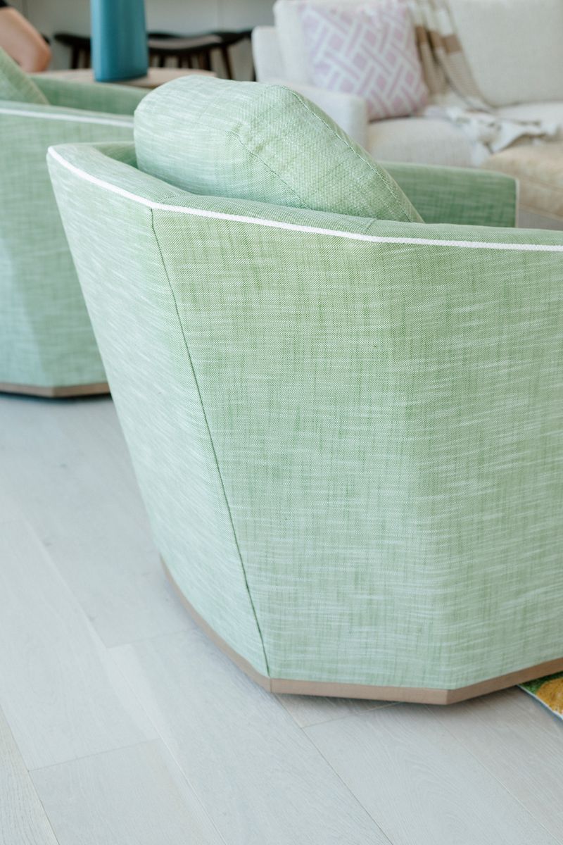 A living room in Panora with a green linen swivel chair trimmed in white welt cord on a pale wood base.