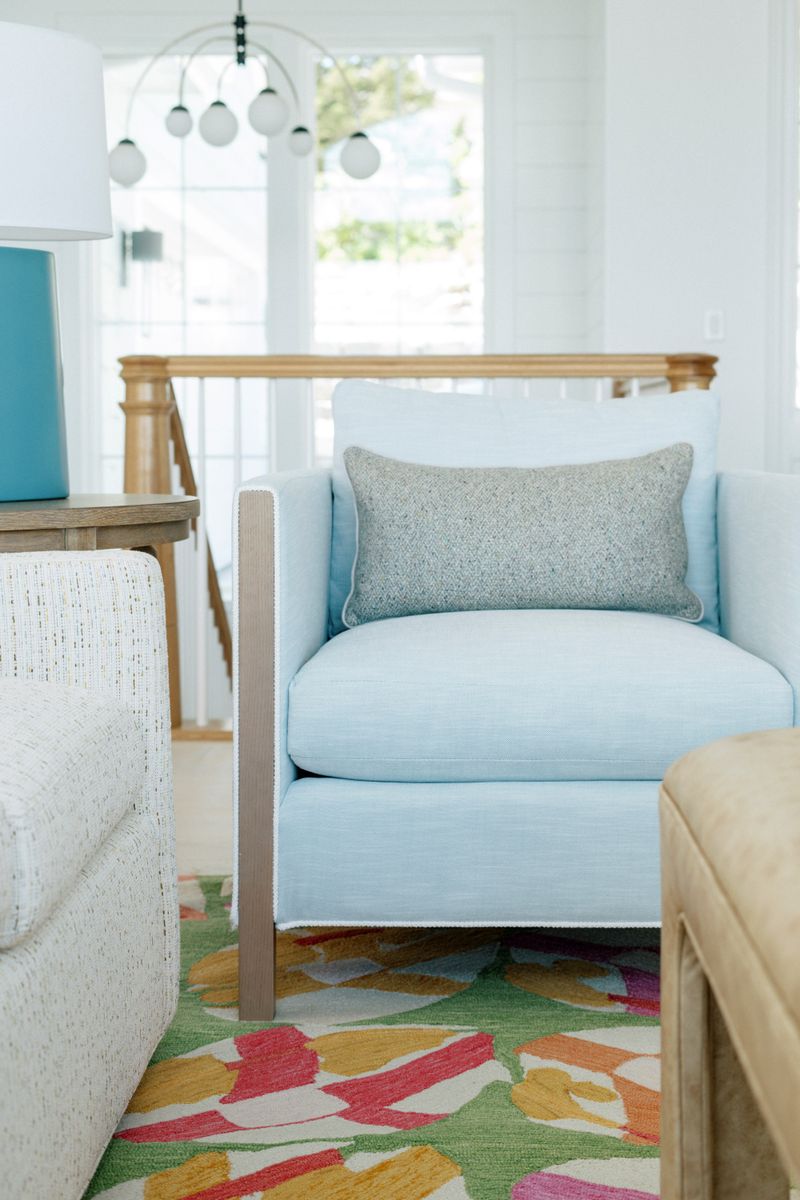 A living room in Panora with a pale blue linen armchair beside an oak stair railing.