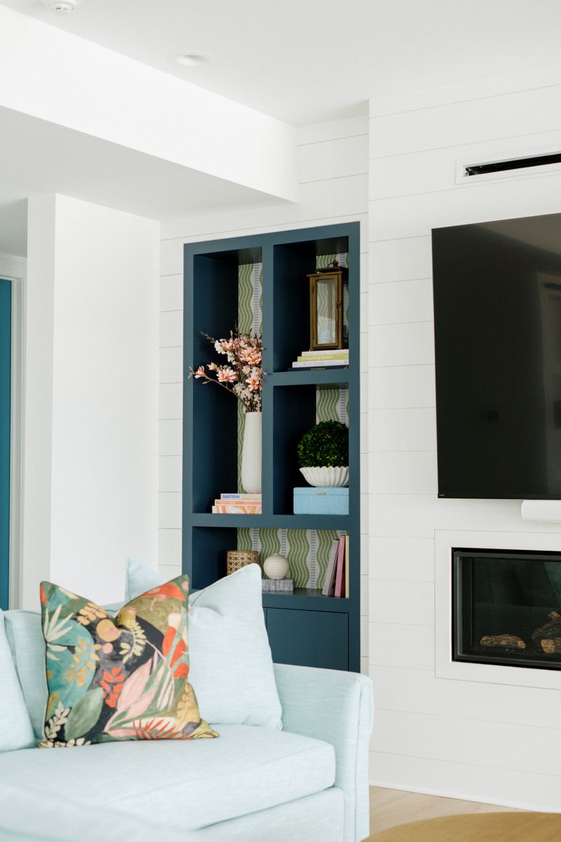 A living room in Panora with a navy built-in bookcase papered in green beside a white shiplap fireplace wall.