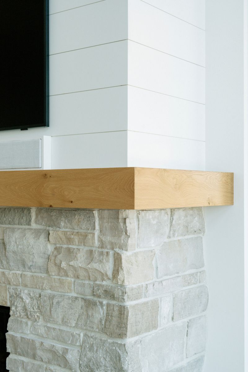 A living room fireplace in Panora with a chunky white oak mantel over pale limestone, under white shiplap.