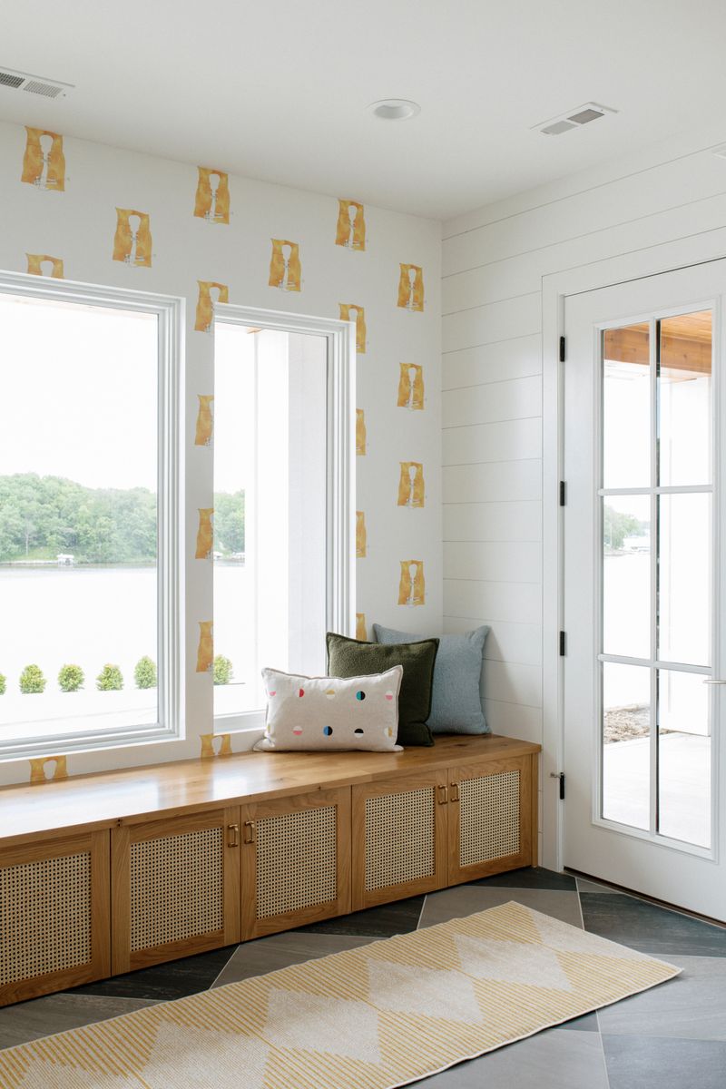 A lakeside mudroom in Panora with a white oak bench under lake house wallpaper and slate tile floors.