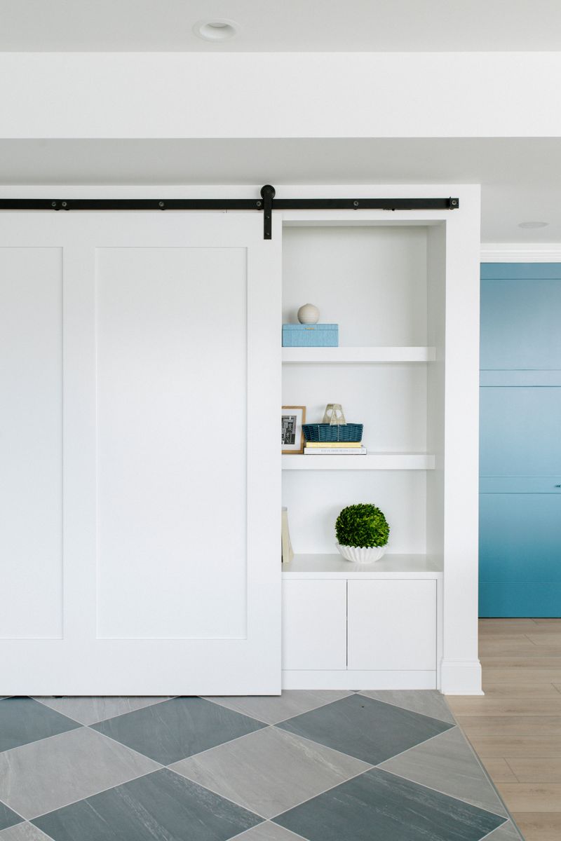 A white mudroom in Panora with a black rail barn door beside gray diamond tile flooring.