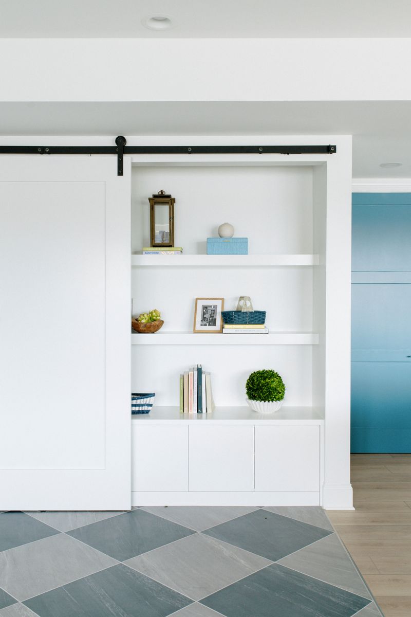 A mudroom in Panora with white built-in shelves behind a sliding barn door and gray diamond tile floors.