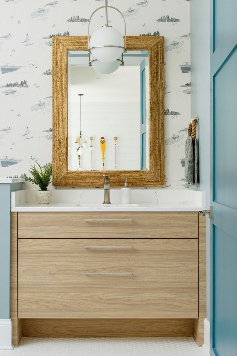 A powder room in Panora with a woven seagrass mirror over a light oak vanity and white quartz counter.