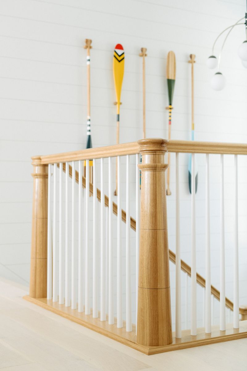A staircase in Panora with white oak railings and painted canoe paddles hung on the shiplap wall.