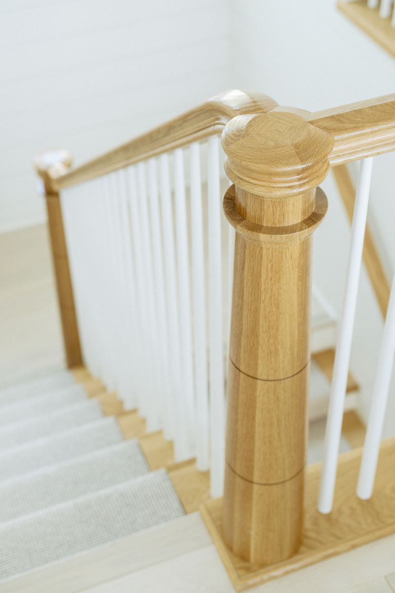 A staircase in Panora with a turned white oak newel post and white spindles above a pale stair runner.