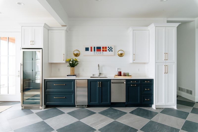 A wet bar in Panora with navy cabinets and brass pulls above a checkerboard gray tile floor.
